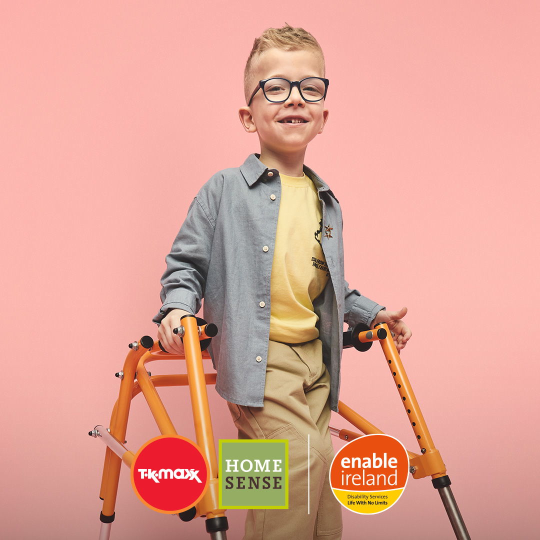 A boy using a walking frame smiles against a pink background.